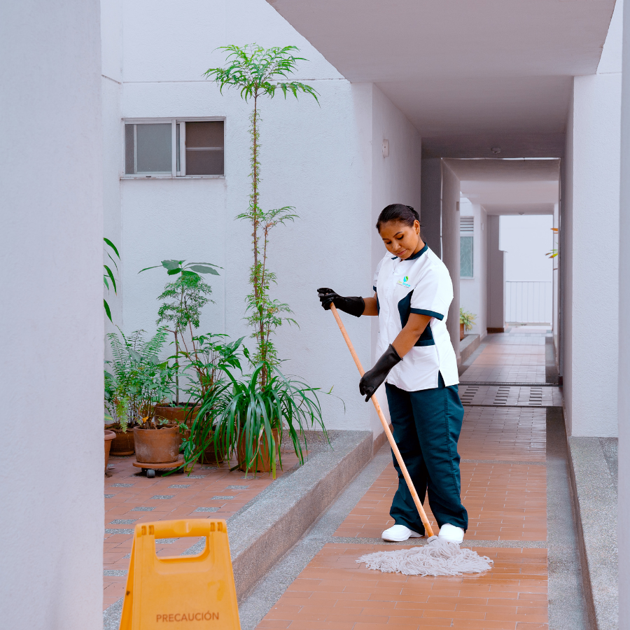 Operaria barriendo camino peatonal y jardines exteriores de un complejo residencial en la ciudad de Cali