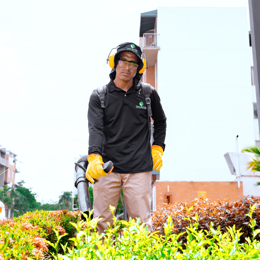 Especialista realizando labores de deshierbe y cuidado de flores de bajo nivel junto a un arbusto topiario con forma espiral.